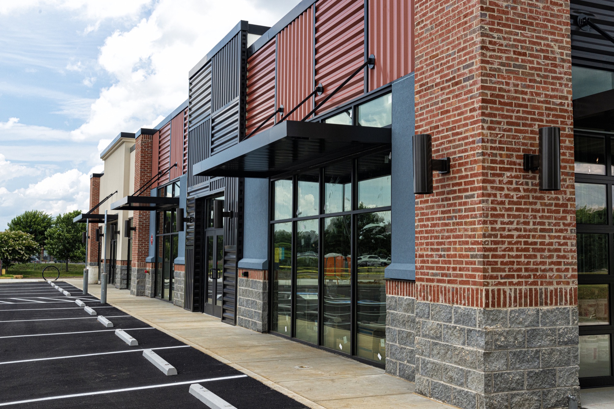 A row of new brick and glass storefronts with black awnings, beside a parking lot